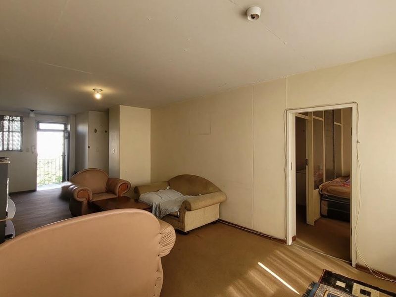A spacious living area featuring carpeted flooring and direct access to an outdoor balcony, offering a blank canvas for renovation and modernization.