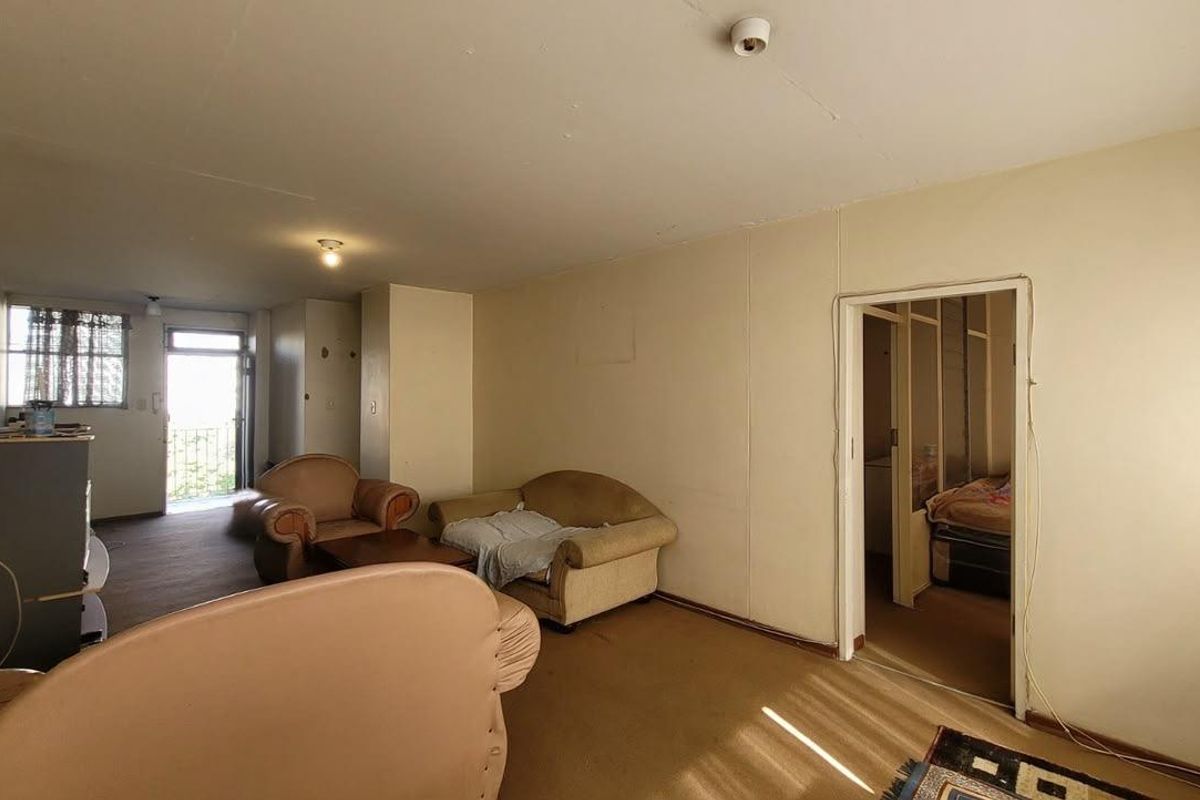 A spacious living area featuring carpeted flooring and direct access to an outdoor balcony, offering a blank canvas for renovation and modernization.