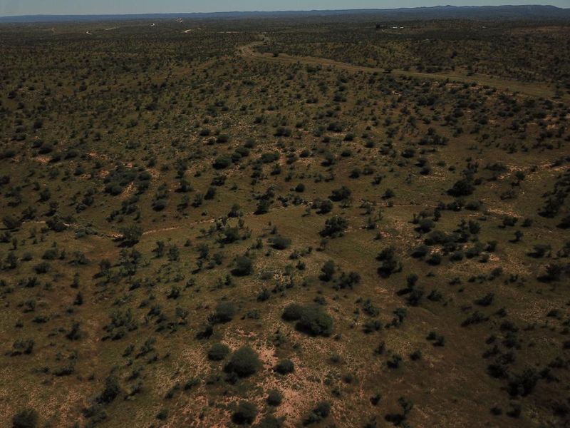 An aerial view of the expansive, undeveloped residential land featuring natural scrub vegetation and a distant access road.