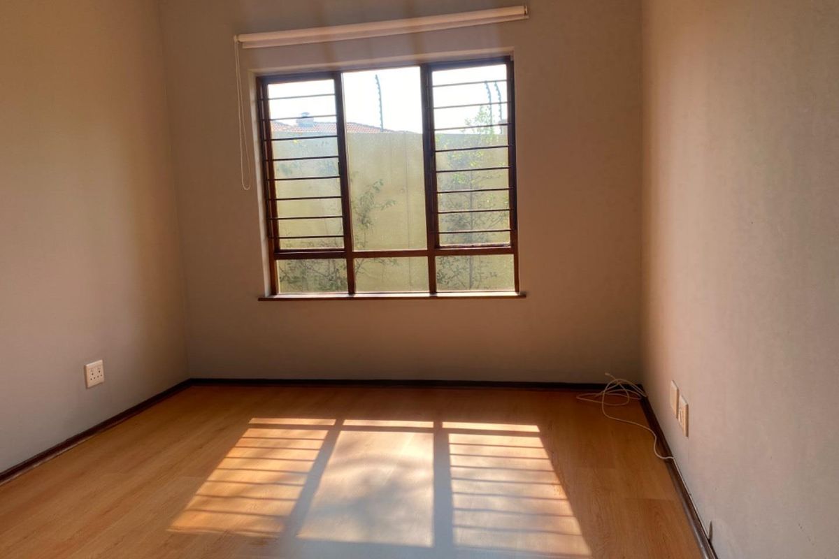 An empty bedroom featuring laminate flooring, security bars on the window, and a neutral wall finish, providing a blank canvas for personalization.