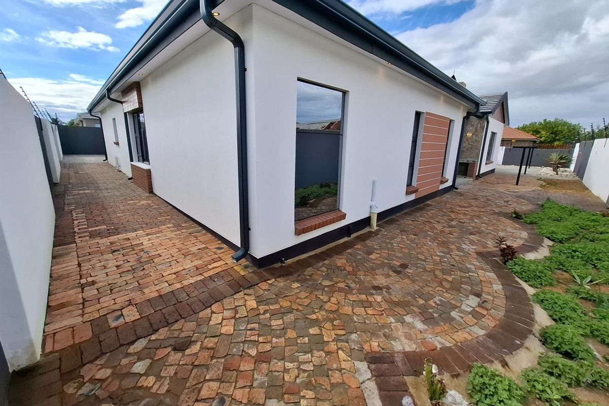 A well-maintained rear exterior featuring decorative brick paving, modern white facade, recessed lighting, and a built-in outdoor braai area.