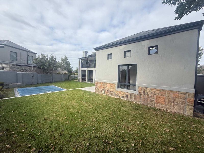 Rear view of the property featuring a landscaped garden, swimming pool with cover, and a modern exterior with stone cladding and plastered walls.
