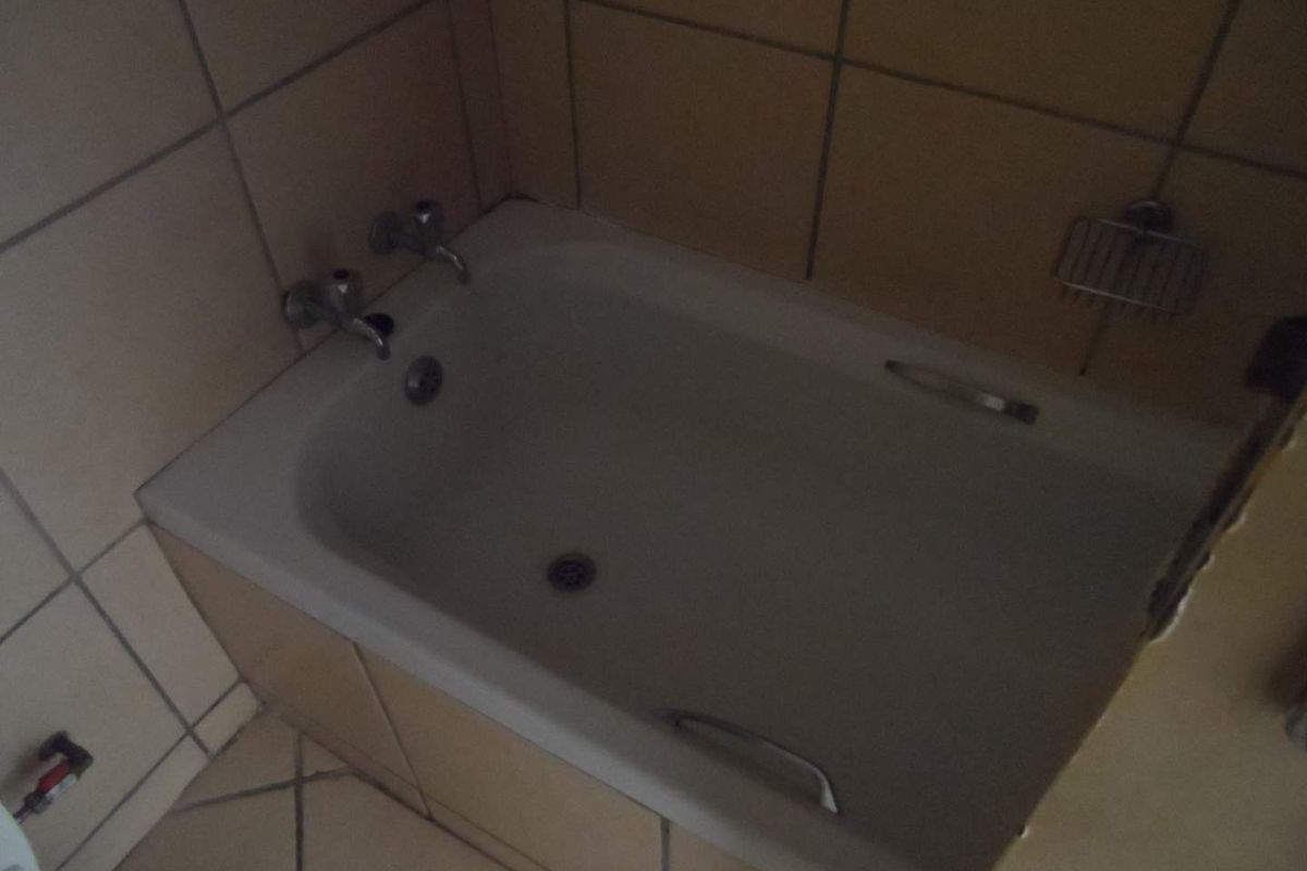 A dated bathroom featuring a built-in bathtub with tiled surround and flooring, requiring cosmetic updates to modernize the space.