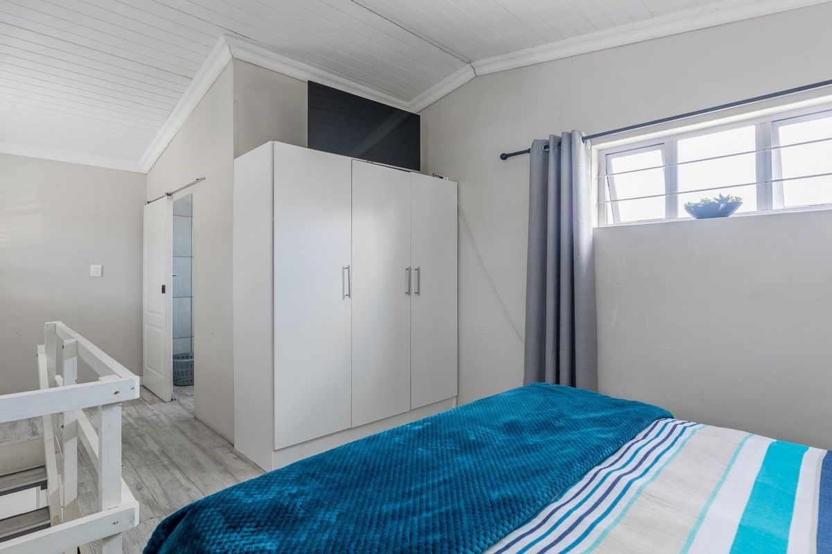 A bright bedroom featuring a built-in wardrobe, timber-look flooring, and a white panelled ceiling, with an adjacent en-suite bathroom visible.