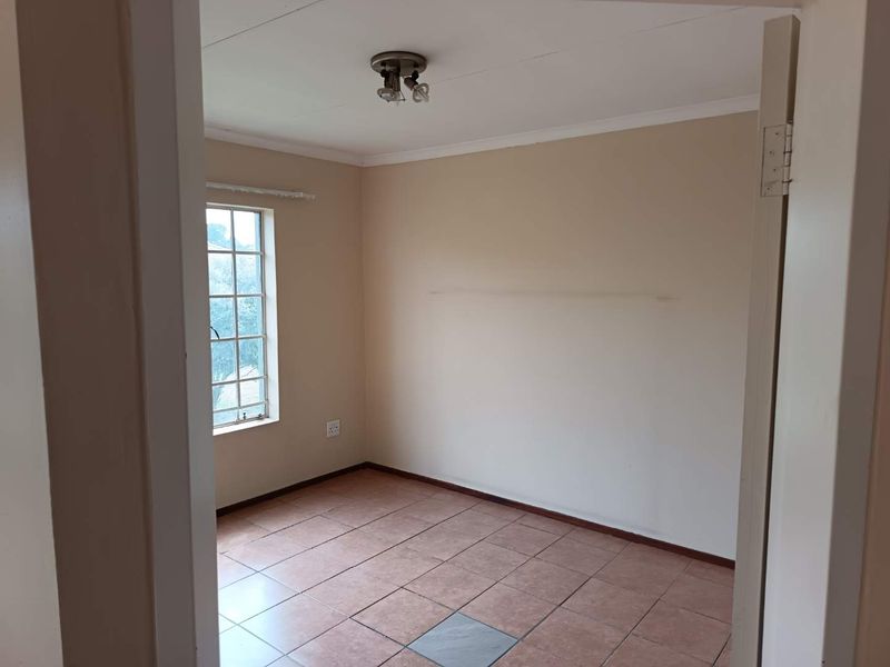 An empty bedroom featuring tiled flooring, a ceiling light fixture, and a window with security bars, ready for personalization.