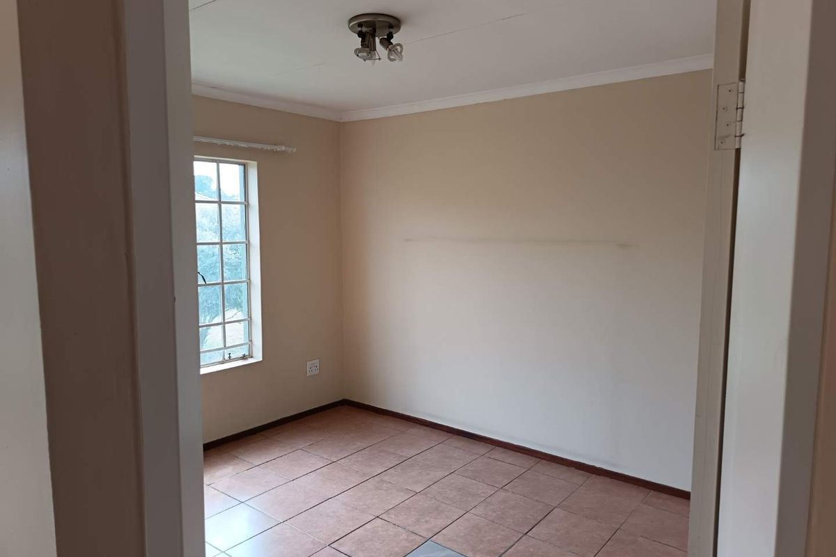 An empty bedroom featuring tiled flooring, a ceiling light fixture, and a window with security bars, ready for personalization.