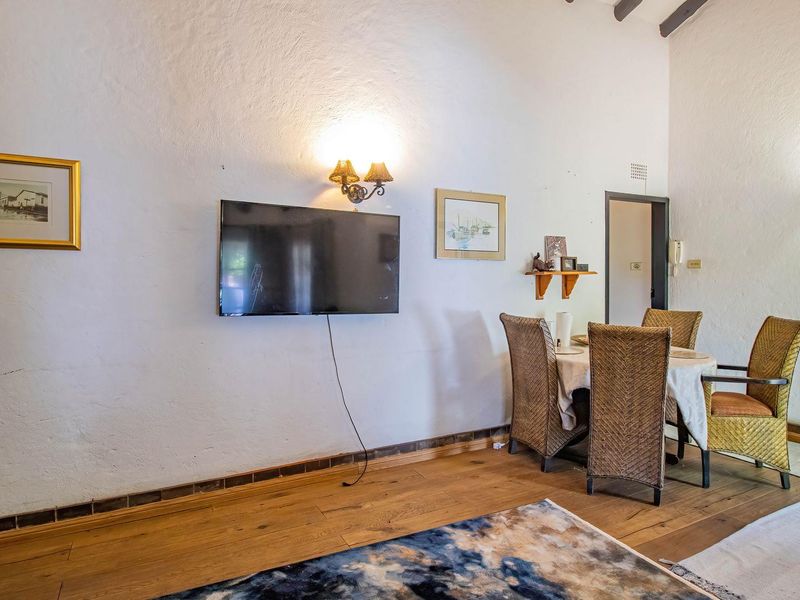 A living area featuring hardwood flooring, exposed ceiling beams, and wall-mounted lighting, offering a rustic aesthetic with potential for modern updates.