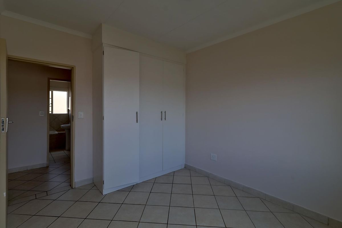 A clean, empty bedroom featuring neutral tiled flooring and white built-in cupboards, with an adjacent view into a bathroom area.