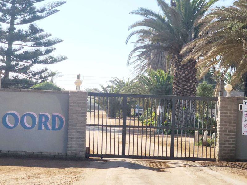 Front entrance view of the property featuring a secure gated access point, brick boundary wall, and established palm trees.