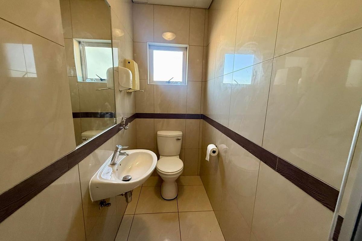 A clean, compact office bathroom featuring tiled walls and flooring, a wall-mounted basin, and a standard toilet.