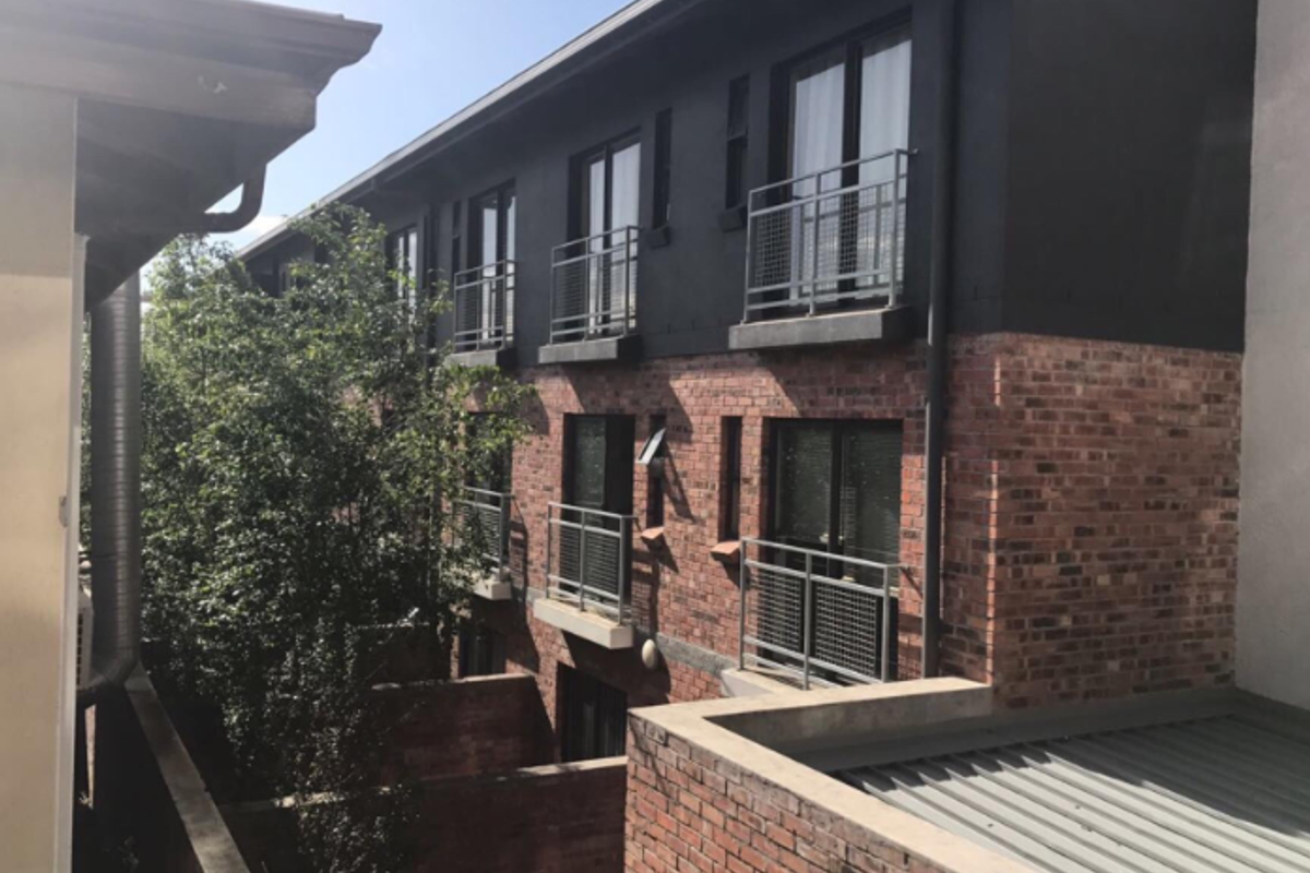 Exterior view of a multi-story apartment building featuring exposed brickwork, dark painted upper levels, and metal balcony railings.