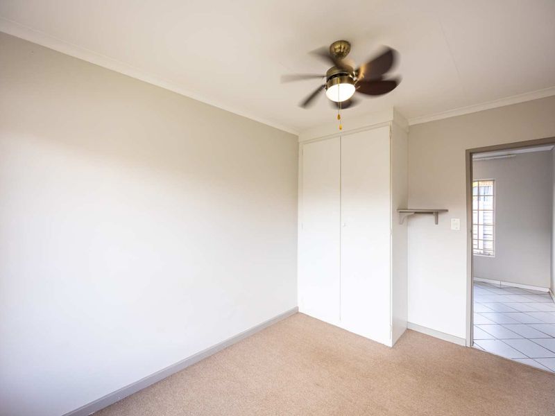 A clean, empty bedroom featuring neutral walls, carpet flooring, a built-in cupboard, and a ceiling fan, offering a blank canvas for personalization.