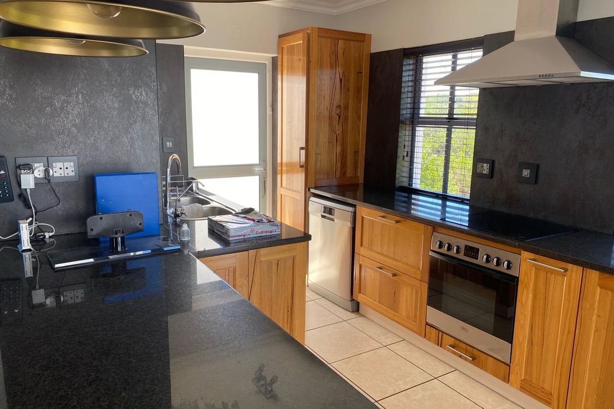 A well-appointed kitchen featuring natural wood cabinetry, dark granite countertops, a stainless steel oven with extractor fan, and tiled flooring.