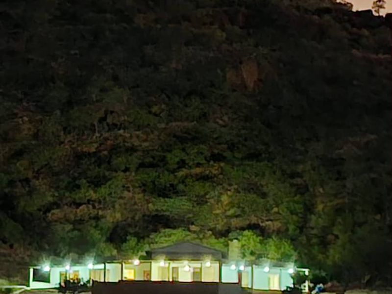 A night view of the property exterior featuring a covered patio area set against a hillside backdrop.