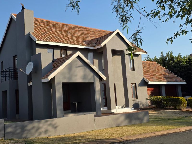 A modern double-story house featuring a grey plastered facade, tiled roof, covered entrance porch, and an attached garage.