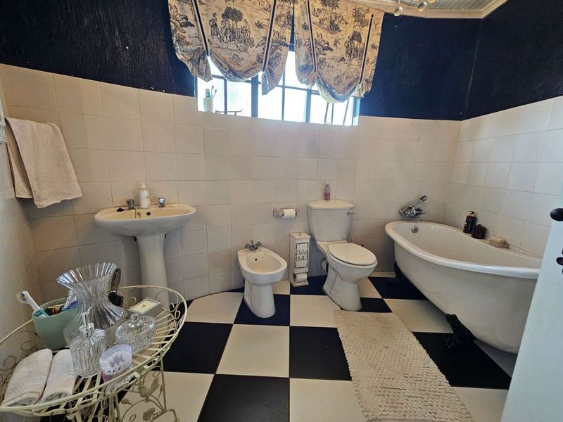 A vintage-style bathroom featuring a clawfoot bathtub, pedestal basin, bidet, and toilet, finished with classic black and white checkered floor tiles.