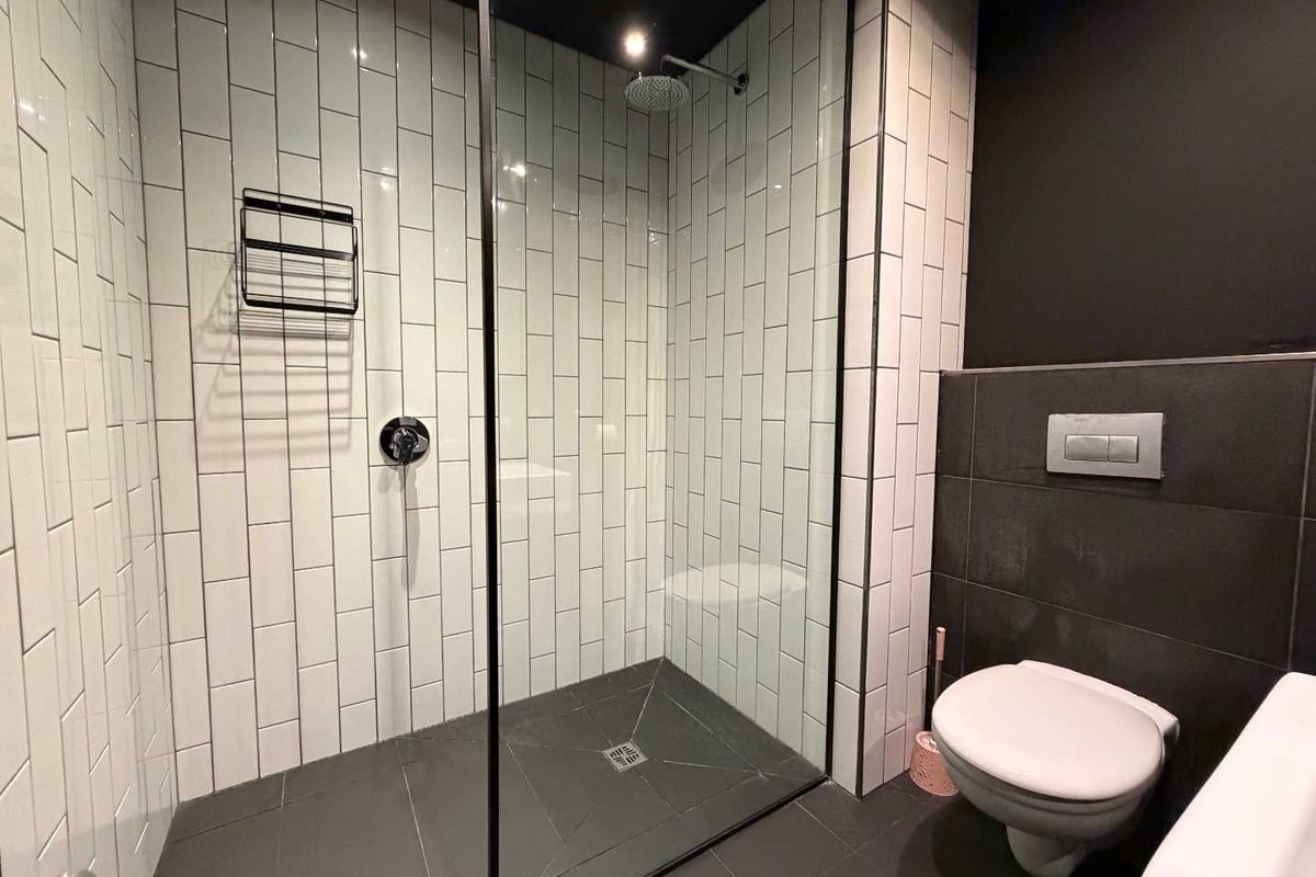 Modern bathroom featuring a walk-in shower with white subway tiles, a glass partition, and a wall-mounted toilet with dark tiled accents.