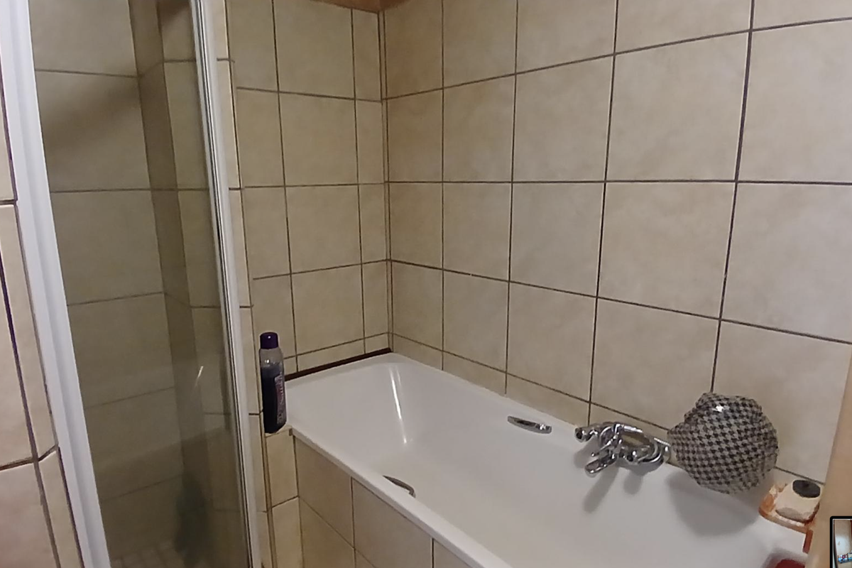 A functional bathroom featuring a built-in bathtub with chrome fixtures and an adjacent glass-enclosed shower stall with neutral wall tiling.