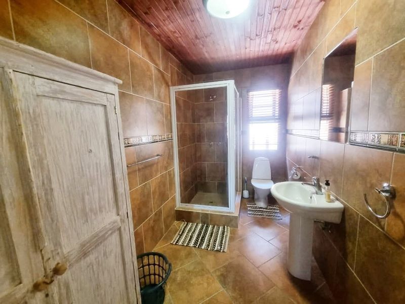 A functional bathroom featuring a pedestal basin, a shower enclosure, and a toilet, finished with brown wall and floor tiles and a timber ceiling.