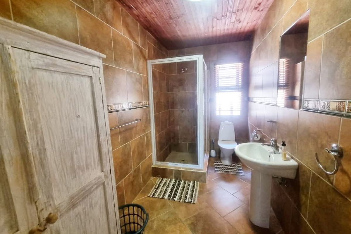 A functional bathroom featuring a pedestal basin, a shower enclosure, and a toilet, finished with brown wall and floor tiles and a timber ceiling.