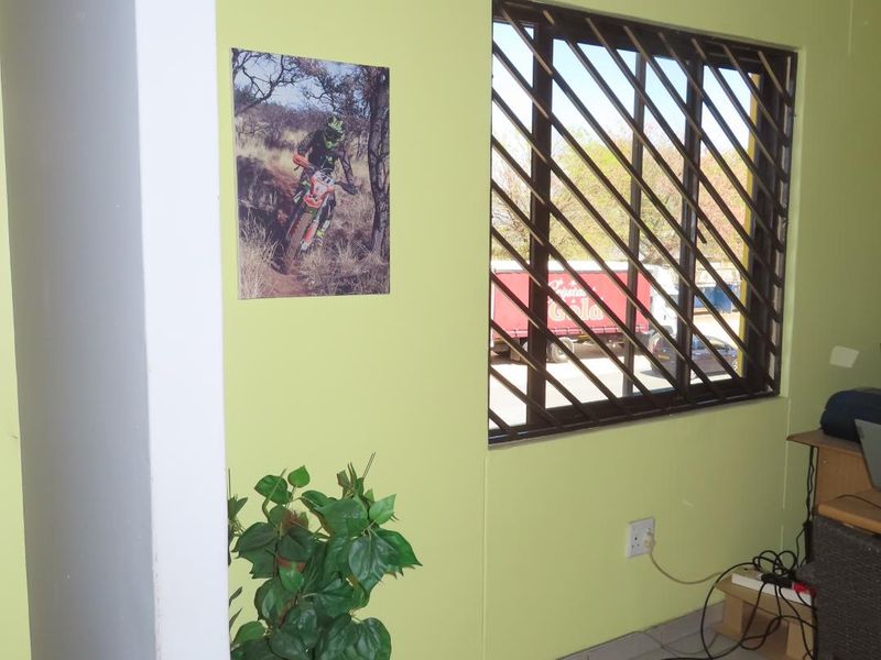 A functional office space featuring tiled flooring, security bars on the window, and visible wall cracking requiring maintenance.