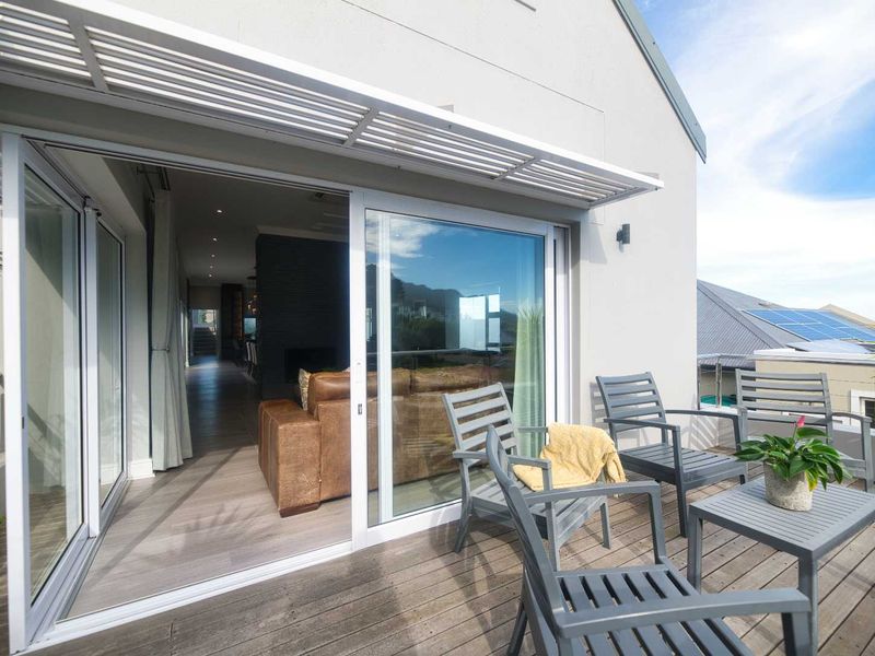 A modern balcony featuring timber decking, a louvred overhead cover, and large sliding glass doors providing seamless access to the interior living space.