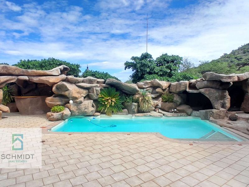 Outdoor pool area featuring a unique rock-sculpted surround, integrated bar area, and extensive paved patio space perfect for entertaining.