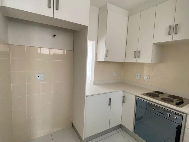A clean, functional kitchen featuring white built-in cabinetry, a tiled backsplash, and integrated electric oven and hob, offering a bright and neutral workspace.