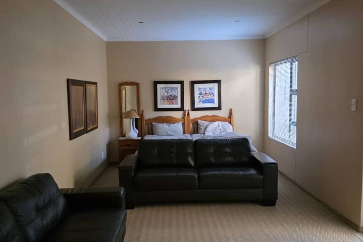 Spacious bedroom featuring neutral wall tones, recessed downlighting, and carpeted flooring, offering a versatile layout for sleeping and seating arrangements.