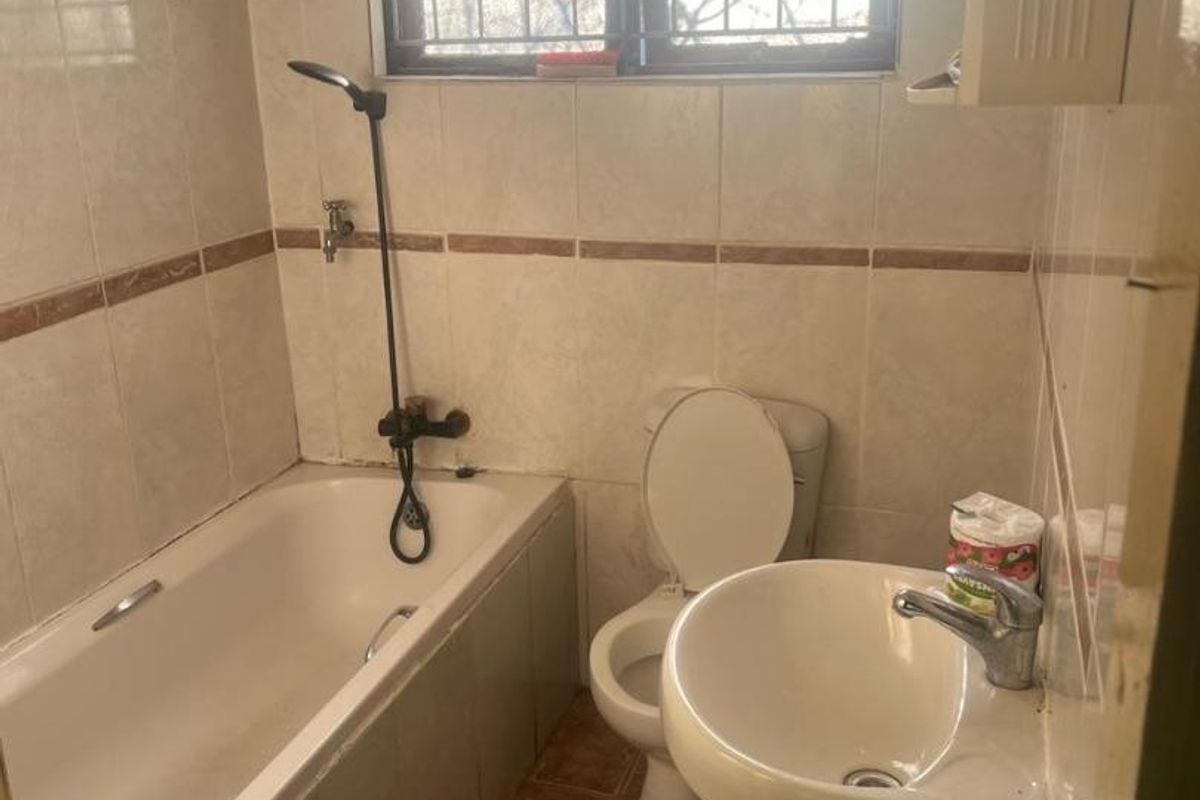 A compact bathroom featuring a bathtub, pedestal basin, and toilet with tiled finishes, requiring modernization to improve its overall aesthetic and functionality.