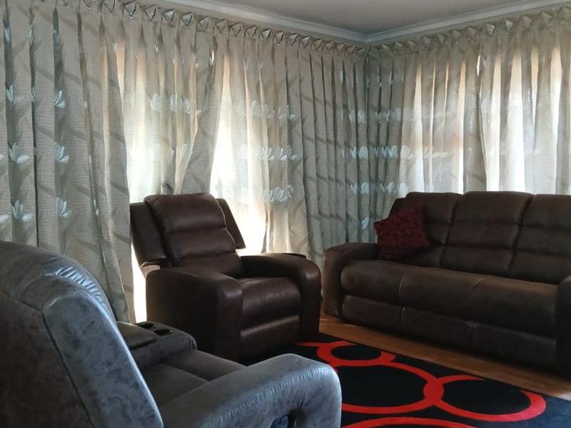 A living room featuring laminate flooring, ceiling cornicing, and full-length window treatments.