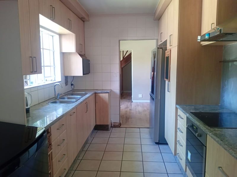 Functional galley-style kitchen featuring light wood cabinetry, granite countertops, built-in oven, and hob, with tiled flooring and backsplash.