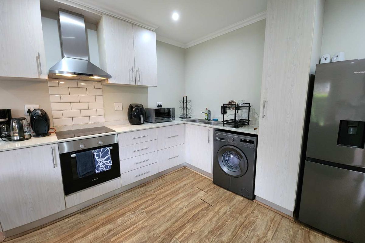 Modern kitchen featuring light wood-grain cabinetry, subway tile backsplash, built-in oven with extractor fan, and integrated laundry appliance space.