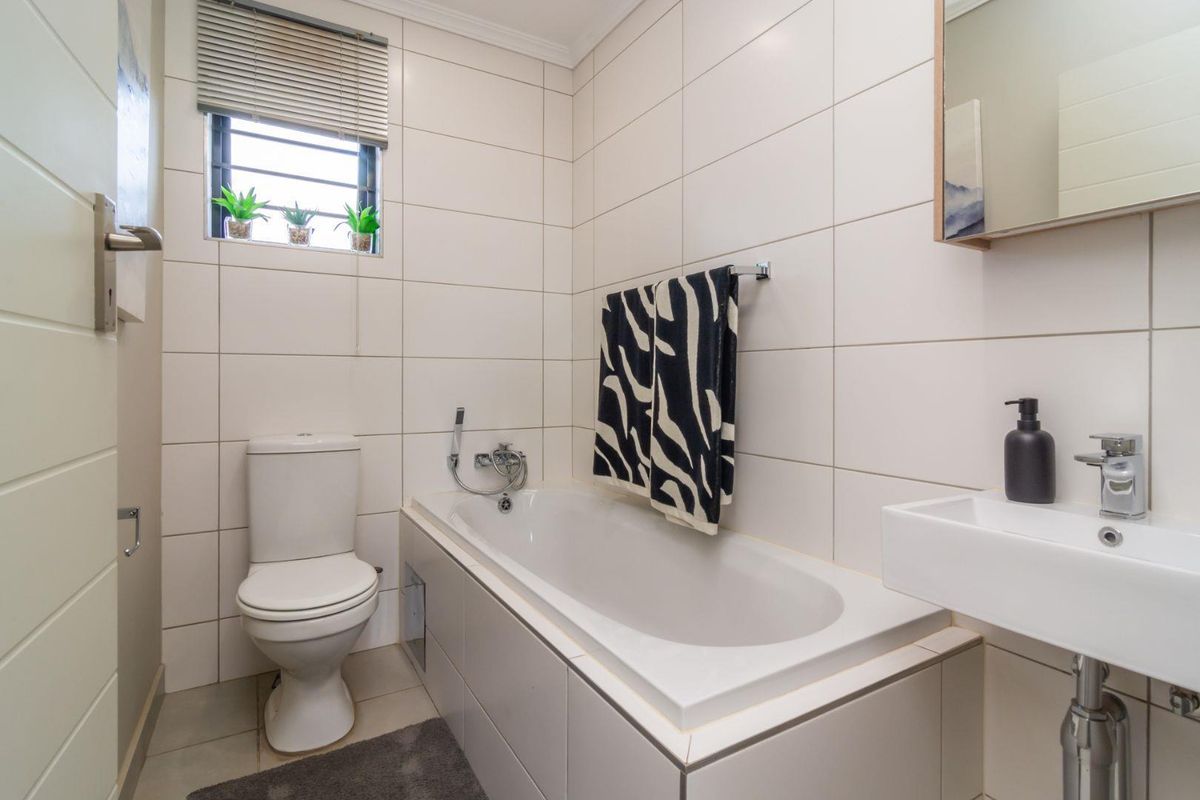 A clean, modern bathroom featuring white wall tiles, a built-in bathtub, a wall-mounted basin, and a standard toilet.