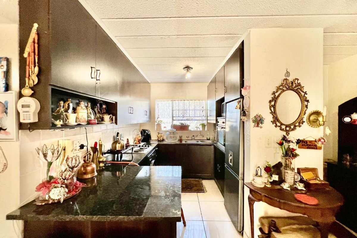A galley-style kitchen featuring dark cabinetry, granite countertops, and tiled flooring, providing a functional workspace with integrated storage and natural light.