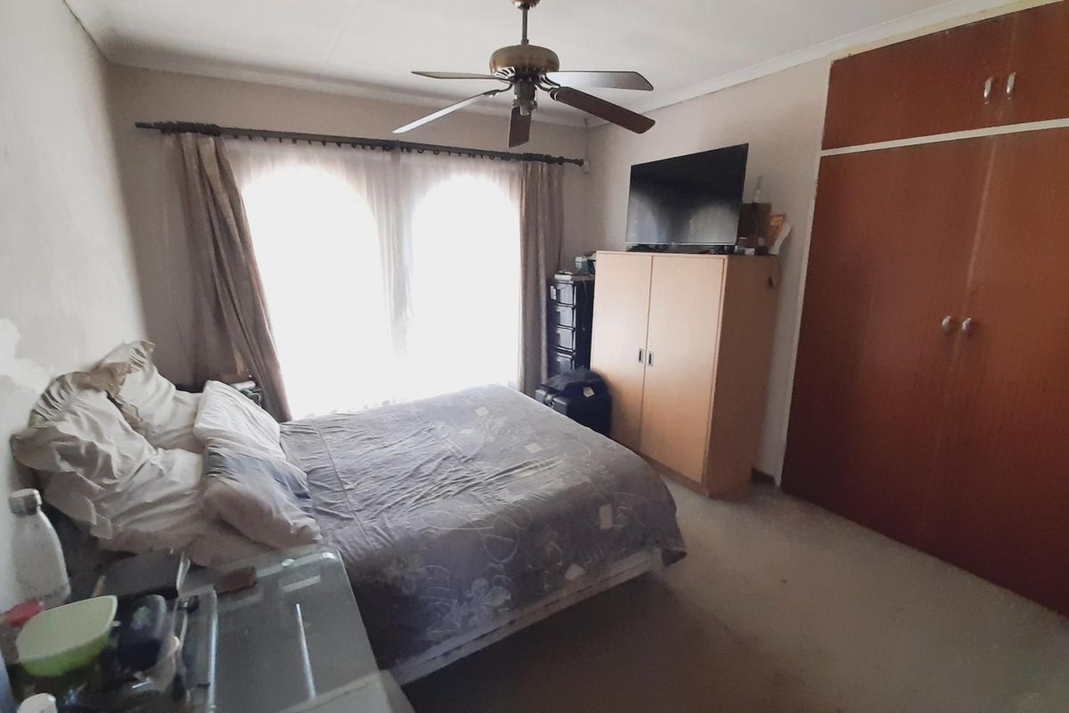 A bedroom featuring built-in wooden cupboards, a ceiling fan, and large windows allowing for natural light.