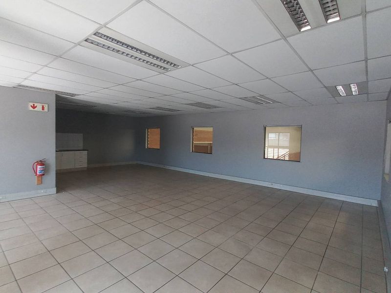 Spacious open-plan industrial office area featuring ceramic tiled flooring, suspended ceiling with recessed lighting, and a small built-in kitchenette corner.