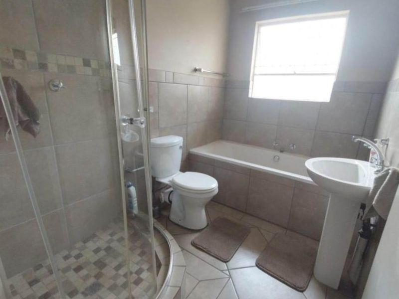A functional bathroom featuring a tiled shower enclosure, pedestal basin, toilet, and a built-in bathtub with neutral wall and floor tiling.