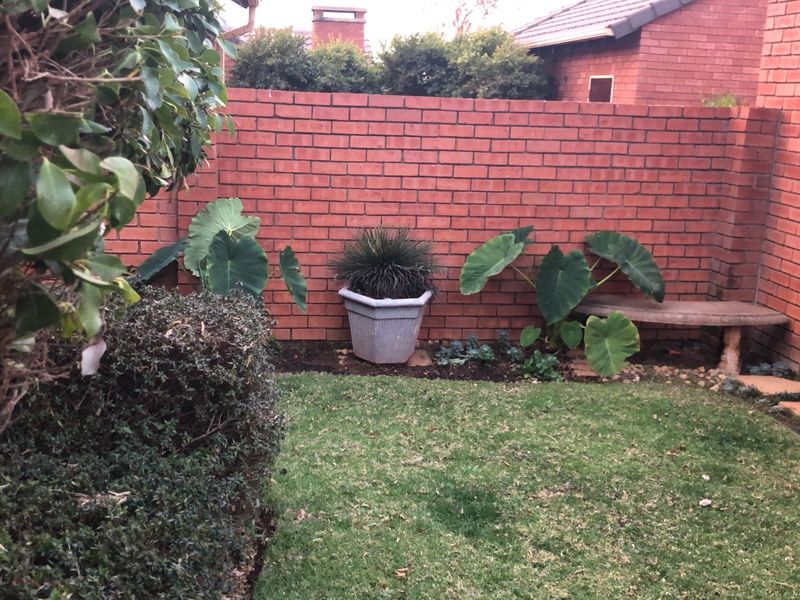 A private rear garden area featuring a well-maintained lawn, established greenery, and a solid brick boundary wall with a built-in stone bench.