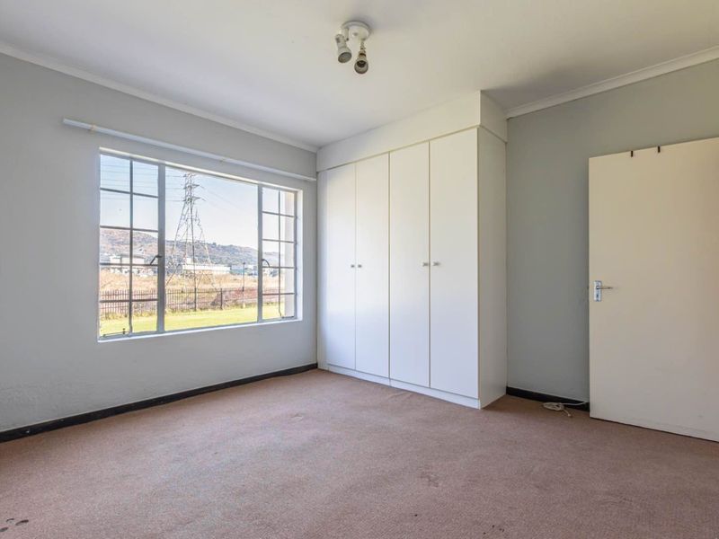 A vacant bedroom featuring built-in cupboards, carpeted flooring, and a large window with views of the surrounding area.