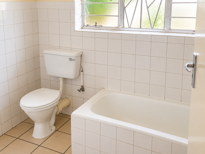 A functional bathroom featuring a built-in bathtub, white wall tiling, and a standard toilet, offering a clean and simple layout.