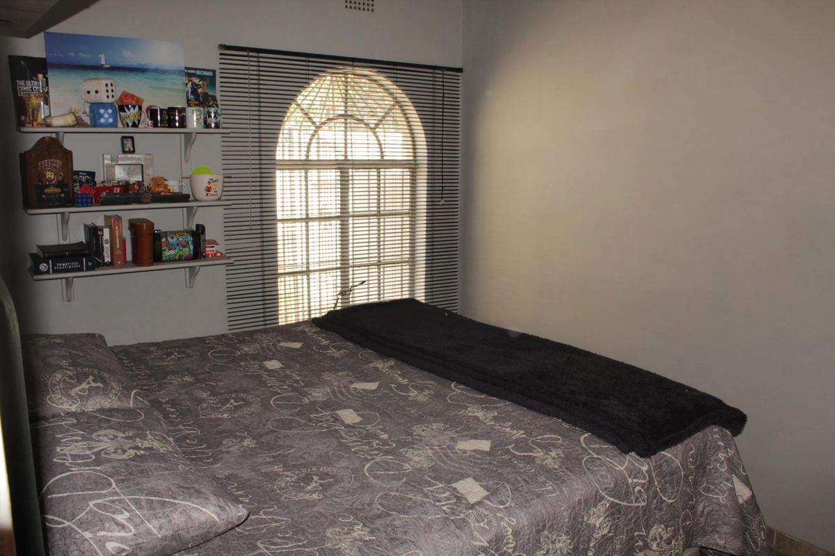 A bedroom featuring a distinctive arched window with fitted blinds and built-in wall shelving.