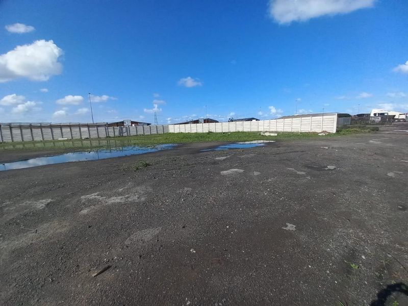 An expansive, undeveloped industrial yard featuring a precast concrete boundary wall and uneven, unpaved ground with visible drainage issues.