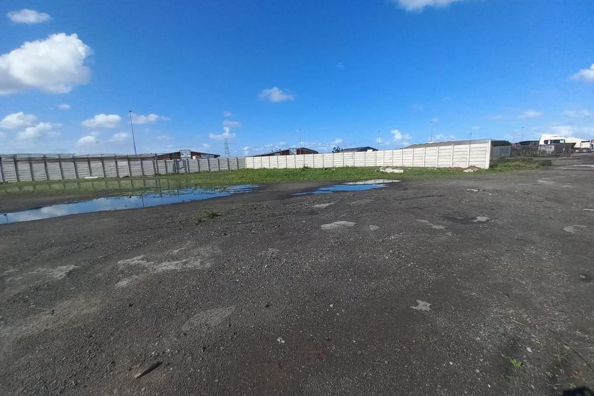 An expansive, undeveloped industrial yard featuring a precast concrete boundary wall and uneven, unpaved ground with visible drainage issues.