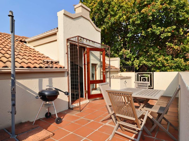 An elevated outdoor patio featuring terracotta tiling, a built-in braai area, and direct access to the interior through a wooden door.