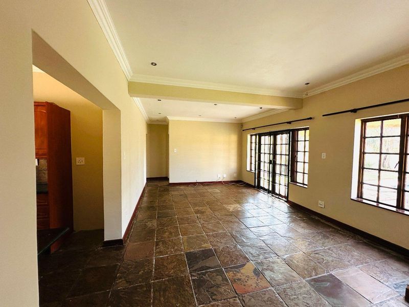 Spacious, empty living area featuring natural slate tile flooring, crown molding, and large sliding glass doors providing access to the exterior.