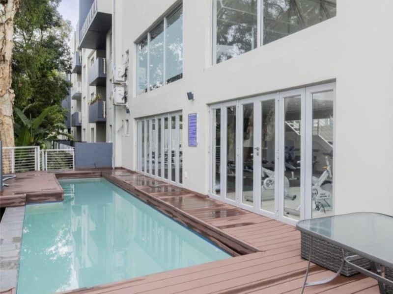 A well-maintained swimming pool area featuring timber decking and large bi-fold glass doors providing access to the building interior.