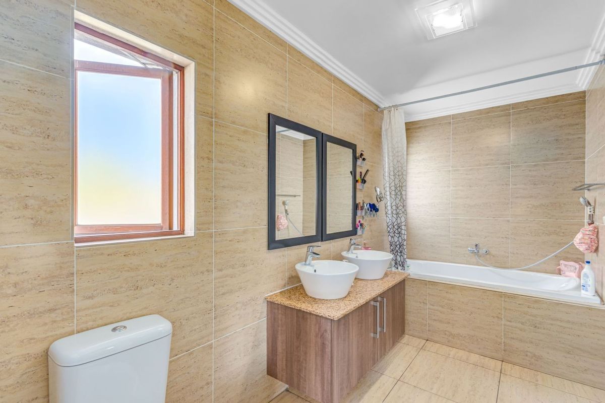A well-maintained bathroom featuring a double vanity with vessel sinks, a built-in bathtub with shower mixer, and neutral floor-to-ceiling wall tiles.