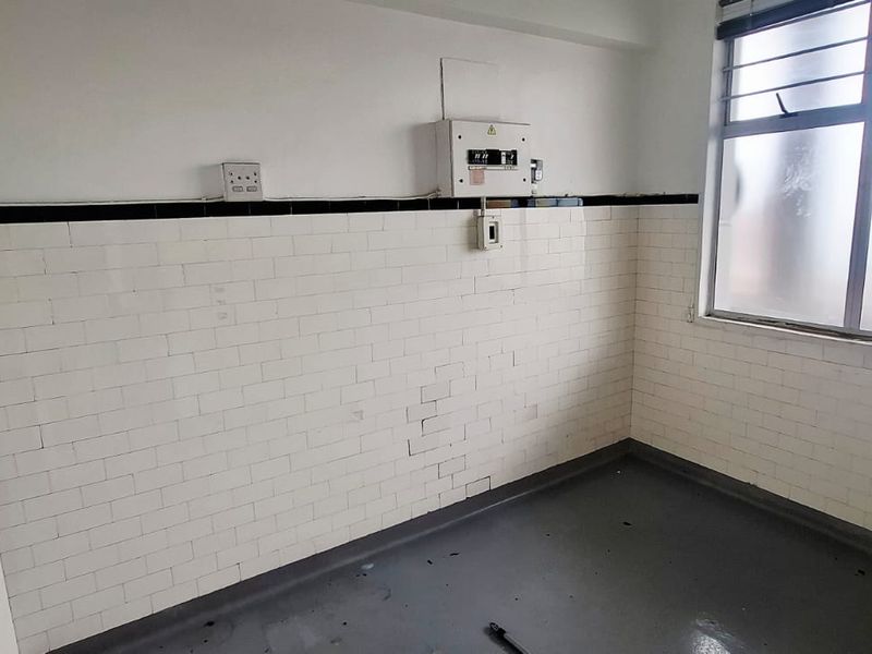 A vacant kitchen area featuring white tiled walls, an electrical distribution board, and an aluminium window, offering a blank canvas for renovation.