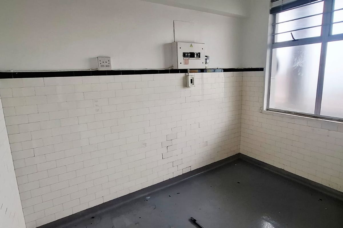 A vacant kitchen area featuring white tiled walls, an electrical distribution board, and an aluminium window, offering a blank canvas for renovation.